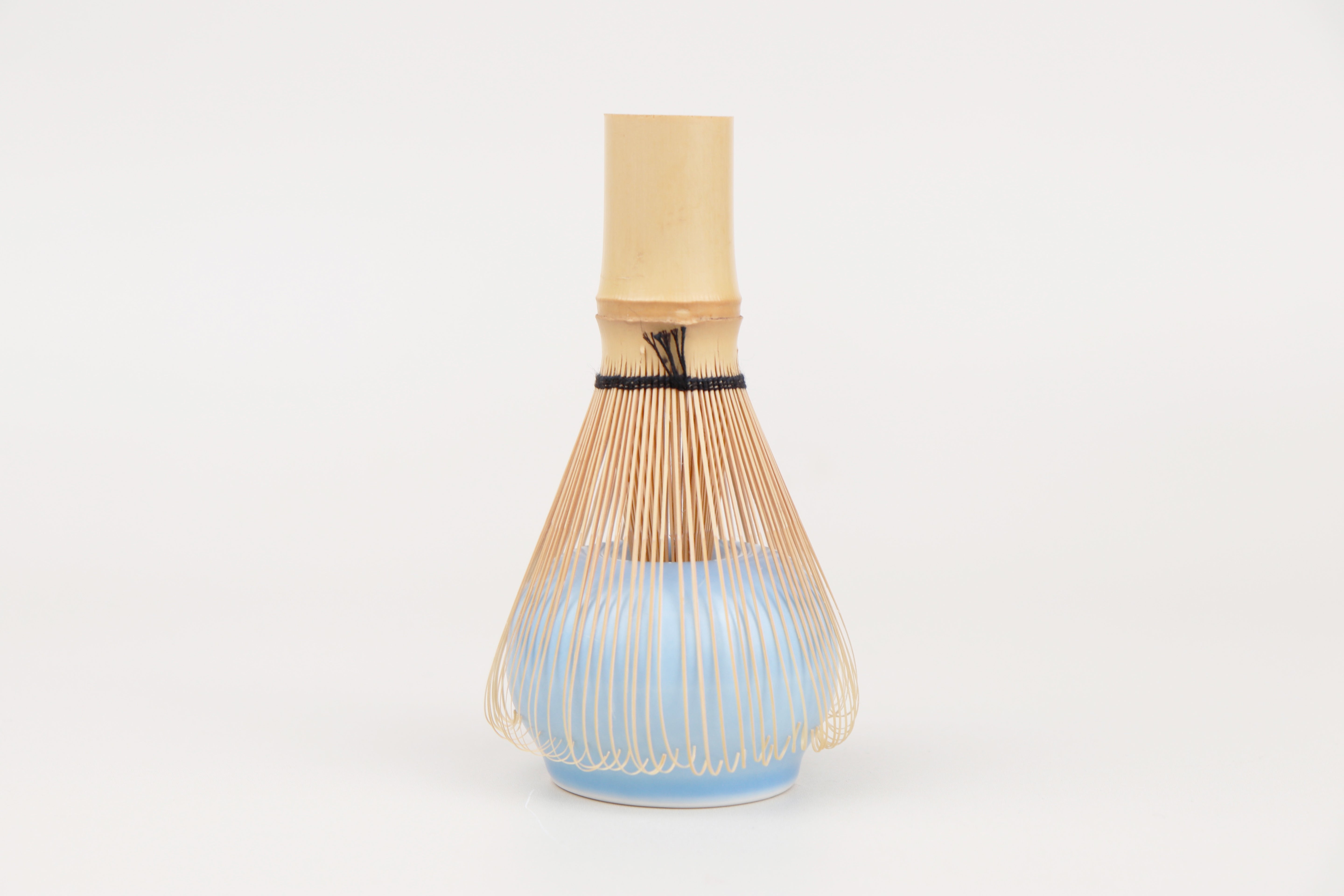 Handcrafted white bamboo chasen resting on a pastel blue ceramic holder, designed to keep your tea whisk in perfect shape for making frothy matcha.